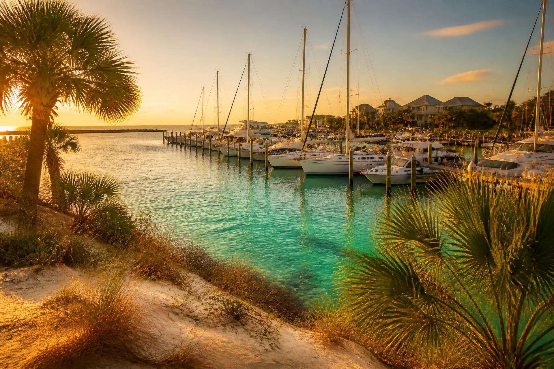 Sunset over a Destin, Florida harbor with sailboats and emerald water